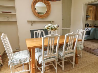 A dining area with a wooden table and six white chairs with checkered seat cushions at Peartree in Colerne