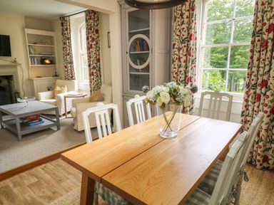 A dining room with a wooden table and white chairs next to a sitting area with armchairs and a coffee table at Peartree in Colerne