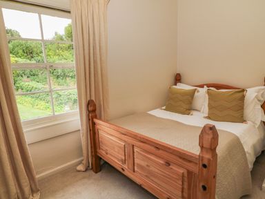 A bedroom with a wooden bed frame two pillows a quilt and a window with beige curtains at Peartree in Colerne