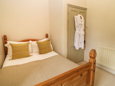 A bedroom with a wooden bed with pillows and beige blanket and a white robe hanging on a door at Peartree in Colerne