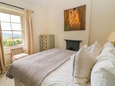 A bedroom with a bed pillows blanket and painting above a fireplace at Peartree in Colerne