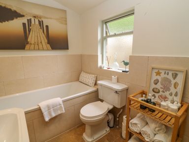 A bathroom with a bathtub toilet wooden shelving unit and window at Peartree in Colerne
