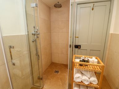 A tiled shower area with glass door next to a wooden rack holding towels and toiletries in a bathroom at Peartree in Colerne
