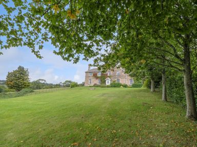 A stone house with bushes and trees on a grassy hill at Peartree in Colerne