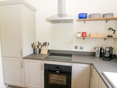 A kitchen with cabinets a stovetop an oven utensils on the counter and shelves with plates and kitchen items at Peartree in Colerne