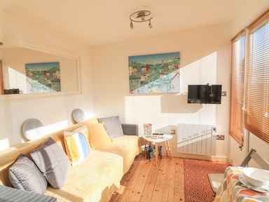 A living room with a yellow sofa with pillows a wall-mounted television a small white table and wooden blinds at 418 Norton Park in Dartmouth