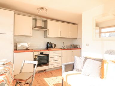 A kitchen with white cabinets a stove microwave kettle toaster and a dining table with a chair at 418 Norton Park Dartmouth