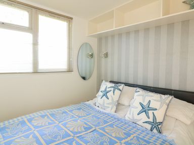 A bedroom with a bed featuring starfish pillows and a blue patterned blanket with windows and an oval mirror on the wall at 418 Norton Park Dartmouth