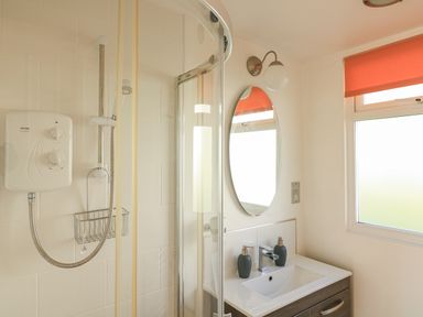 A bathroom with a shower enclosure, oval mirror, sink with two soap dispensers, and a window with an orange blind at 418 Norton Park in Dartmouth