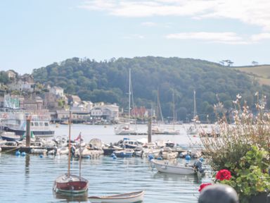 A harbor with boats and yachts docked near a town and wooded hills with flowers in the foreground at 418 Norton Park in Dartmouth