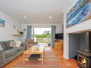 A living room with a sofa armchair coffee table and wood stove at Bryher in Trebetherick near Polzeath