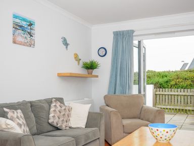 A living room with a sofa armchair coffee table and open glass door leading to a garden at Bryher in Trebetherick near Polzeath