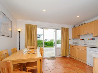 A kitchen dining area with wooden table and chairs near glass doors and kitchen cabinets at Bryher in Trebetherick near Polzeath