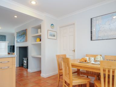 A dining area with wooden chairs and table set with teapot and cups next to a kitchen with tiled floor at Bryher in Trebetherick near Polzeath