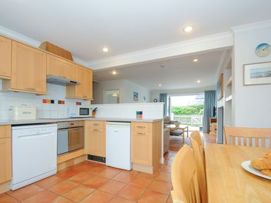 A kitchen with wooden cabinets dishwasher oven microwave and dining table with chairs at Bryher Trebetherick near Polzeath