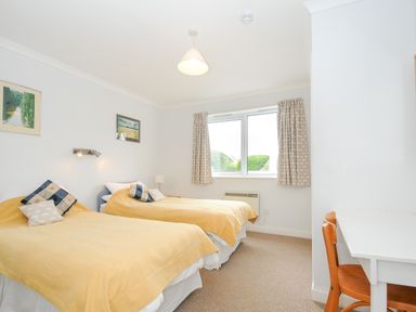 A bedroom with two single beds with yellow bedspreads a window a white desk and a wooden chair at Bryher Trebetherick near Polzeath