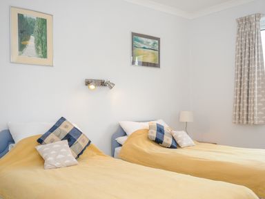 A bedroom with two single beds covered with yellow bedspreads and pillows at Bryher in Trebetherick near Polzeath