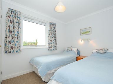 A bedroom with two single beds covered with light blue blankets and a wooden nightstand between them at Bryher in Trebetherick near Polzeath