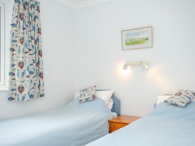 A bedroom with two single beds blue blankets fish patterned curtains and pillows and a wooden nightstand Bryher Trebetherick near Polzeath