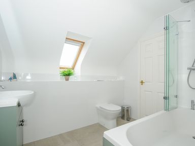 A bathroom with a bathtub shower combination a toilet a sink a small window and a plant at Bryher in Trebetherick near Polzeath