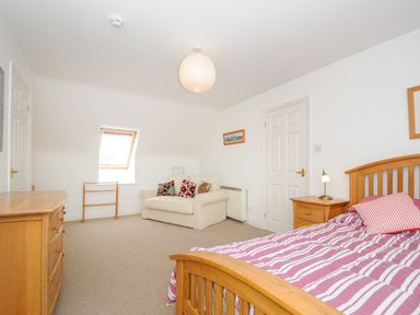 A bedroom with a wooden bed bedside table sofa chest of drawers and a window at Bryher in Trebetherick near Polzeath