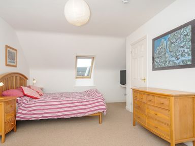 A bedroom with a wooden bed red striped bedding wooden dresser and bedside table with framed pictures on walls at Bryher in Trebetherick near Polzeath