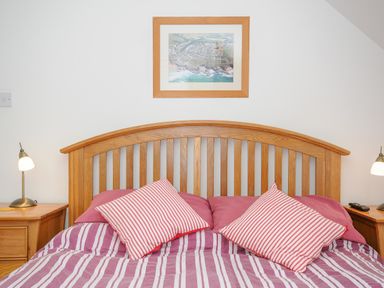 A bedroom with a wooden headboard bed two bedside tables with lamps and a framed photo on the wall at Bryher in Trebetherick near Polzeath
