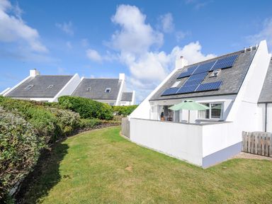 A white house with solar panels on the roof and a patio umbrella in a garden with trimmed bushes at Bryher in Trebetherick near Polzeath