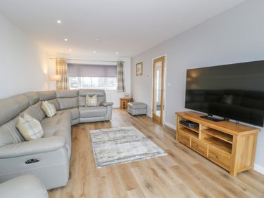 A living room with a grey sectional sofa a wooden TV stand and a large flat screen TV at Melin Y Plas in Llanaber