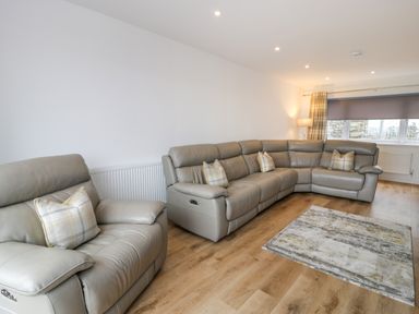 A living room with a gray leather sofa set wood flooring and a patterned rug at Melin Y Plas in Llanaber