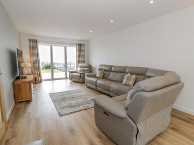 A living room with leather sofas a wooden TV stand and sliding glass doors leading outside at Melin Y Plas in Llanaber