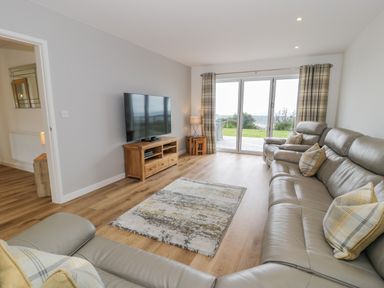A living room with leather sofas and a television on a wooden stand at Melin Y Plas in Llanaber