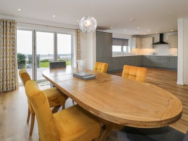 A dining area with a wooden table and yellow and gray chairs next to a kitchen with gray cabinets at Melin Y Plas in Llanaber
