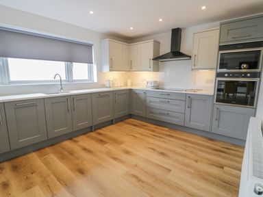 A kitchen with grey and white cabinets wooden floor and appliances at Melin Y Plas in Llanaber
