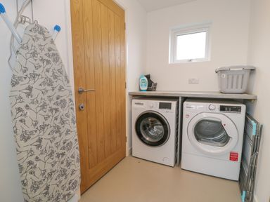 A laundry room with a washing machine dryer ironing board and laundry basket at Melin Y Plas in Llanaber