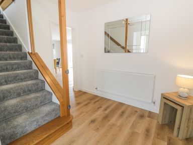 A hallway with carpeted stairs wooden banister a wall mirror radiator wooden floor and a small table with a lamp at Melin Y Plas in Llanaber