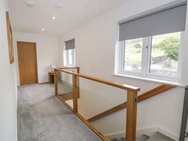A hallway with gray carpet wooden door windows and a staircase with wooden and glass railing at Melin Y Plas in Llanaber