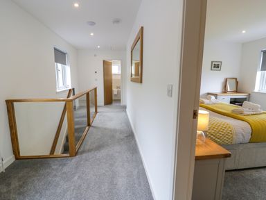 A hallway with carpet leading to a bathroom and a bedroom with a bed and a bedside lamp at Melin Y Plas in Llanaber