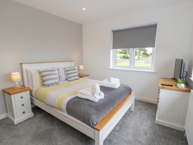 A bedroom with a bed two bedside tables lamps a window with a blind and a cabinet with a television at Melin Y Plas in Llanaber
