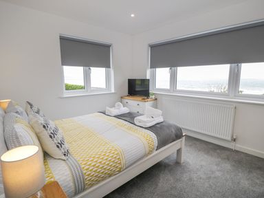 A bedroom with a double bed, bedside lamp, chest of drawers with a television, and windows with grey blinds at Melin Y Plas in Llanaber