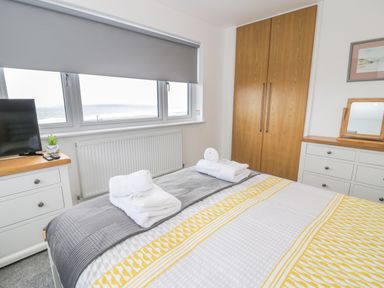 A bedroom with a bed with folded towels a window with grey blinds and a wooden wardrobe at Melin Y Plas in Llanaber