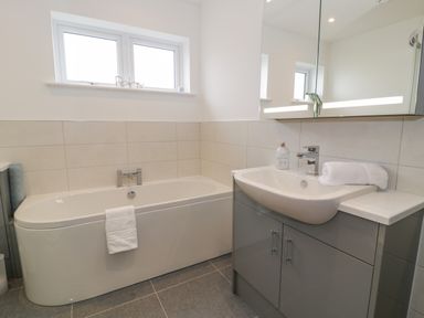 A bathroom with a bathtub and a sink with a cabinet under a mirror at Melin Y Plas in Llanaber