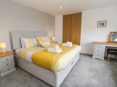 A bedroom with a large bed with yellow and white bedding two bedside tables with lamps a wooden wardrobe and a dressing table with a mirror at Melin Y Plas in Llanaber