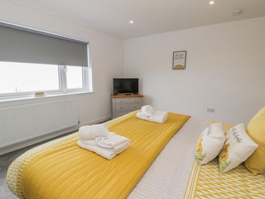 A bedroom with a yellow bedspread and folded towels and a small television on a dresser at Melin Y Plas in Llanaber