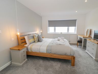 A bedroom with a wooden bed frame a gray carpet and bedside tables at Melin Y Plas in Llanaber