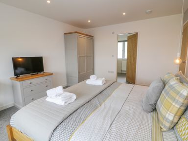 A bedroom with a bed dressed in patterned bedding and pillows a TV on a dresser and a wardrobe at Melin Y Plas in Llanaber