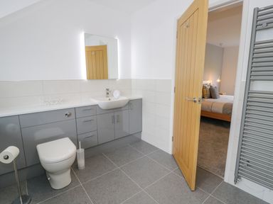 A bathroom with a toilet sink and gray cabinets next to an open door leading to a bedroom at Melin Y Plas in Llanaber