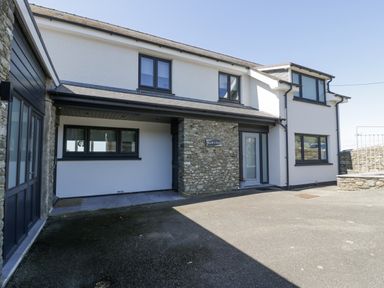 The exterior front view of a white two-story house with black-framed windows and a stone wall section at Melin Y Plas in Llanaber