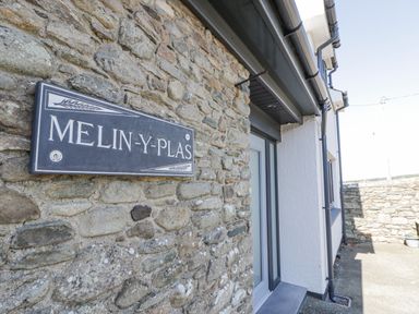 Stone wall with a Melin Y Plas sign next to a doorway and paved area outside at Melin Y Plas in Llanaber