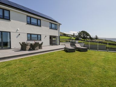 A garden with sun loungers and outdoor dining set next to a two story house with solar panels at Melin Y Plas in Llanaber